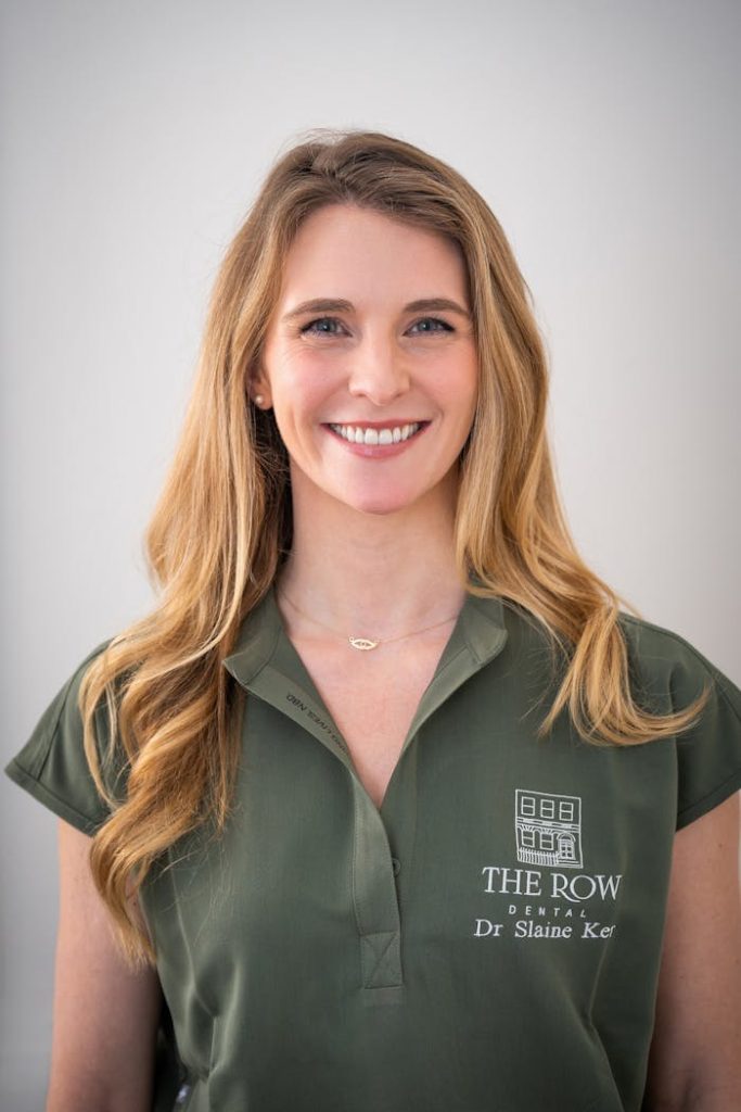 Portrait of a smiling female dentist in a green uniform, offering dental services.